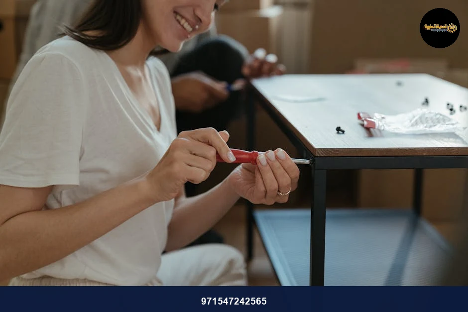 Woman smiling while assembling a table using a screwdriver in a home setting.