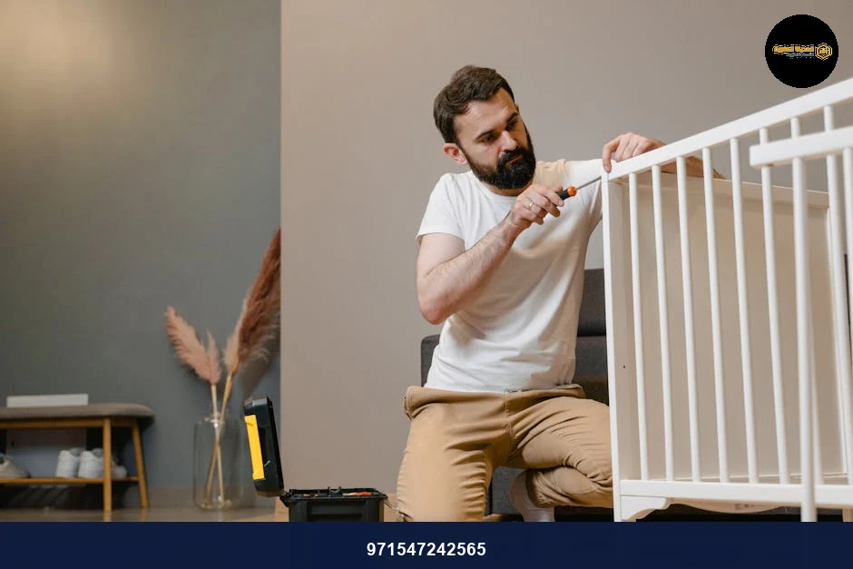 Father kneels to fix a white baby crib using a screwdriver in a contemporary nursery setting.