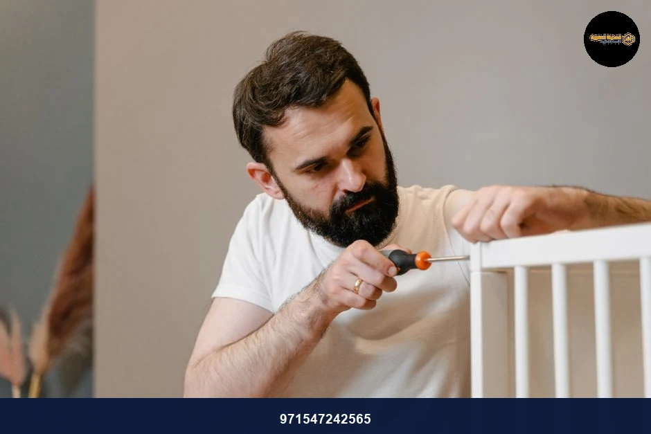 A man focusing closely on assembling a baby crib with a screwdriver in a well-lit room.