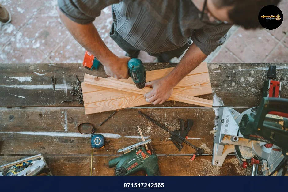 Craftsman busy drilling wooden planks in a carpentry workshop with various tools around.