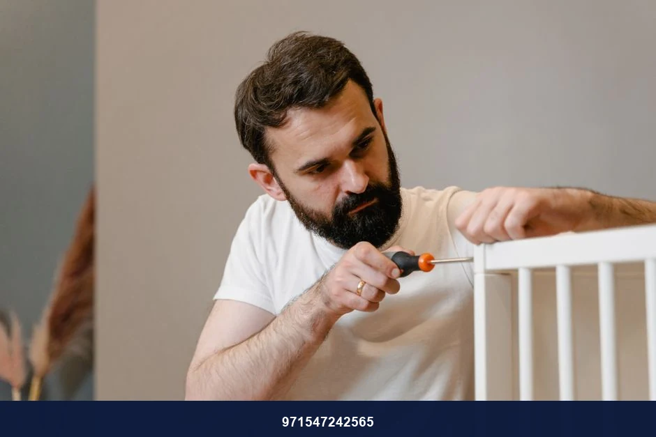 A man focusing closely on assembling a baby crib with a screwdriver in a well-lit room. A man focusing closely on assembling a baby crib with a screwdriver in a well-lit room.