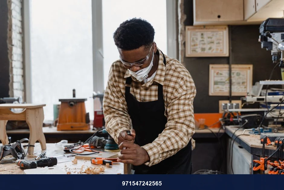 An African American craftsman focuses on woodworking in a well-equipped workshop.