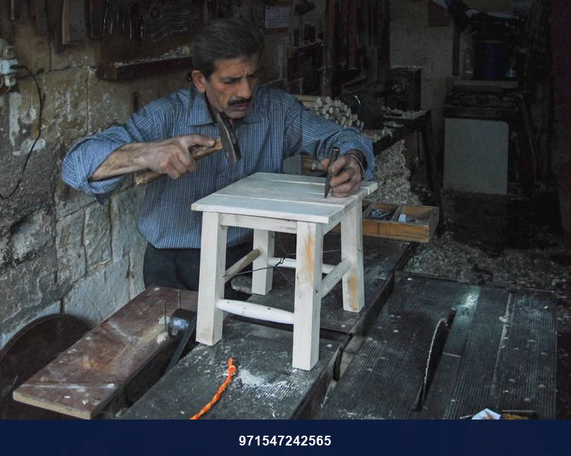 A carpenter skillfully crafting a wooden stool in his workshop using hand tools.