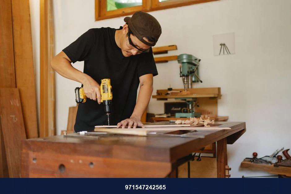 Focused man in cap standing near workbench and drilling hole in plank while repairing wooden detail