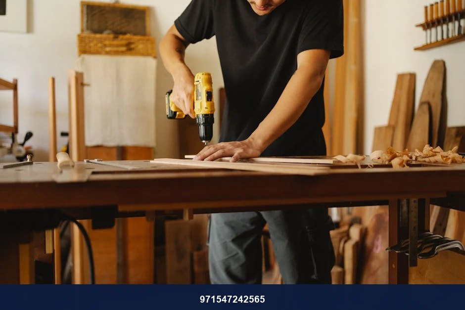 Crop anonymous man in casual clothes standing near workbench and drilling while working in joinery