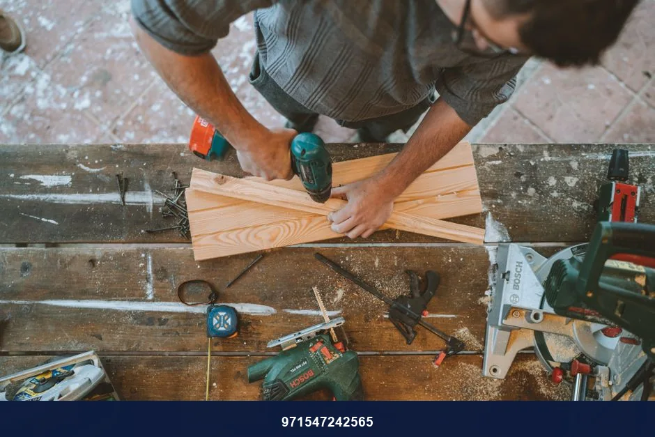 Craftsman busy drilling wooden planks in a carpentry workshop with various tools around.