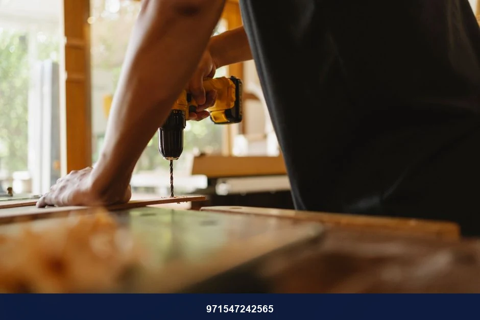 Crop anonymous male carpenter making hole on wooden plank with drill during work in studio on sunny day