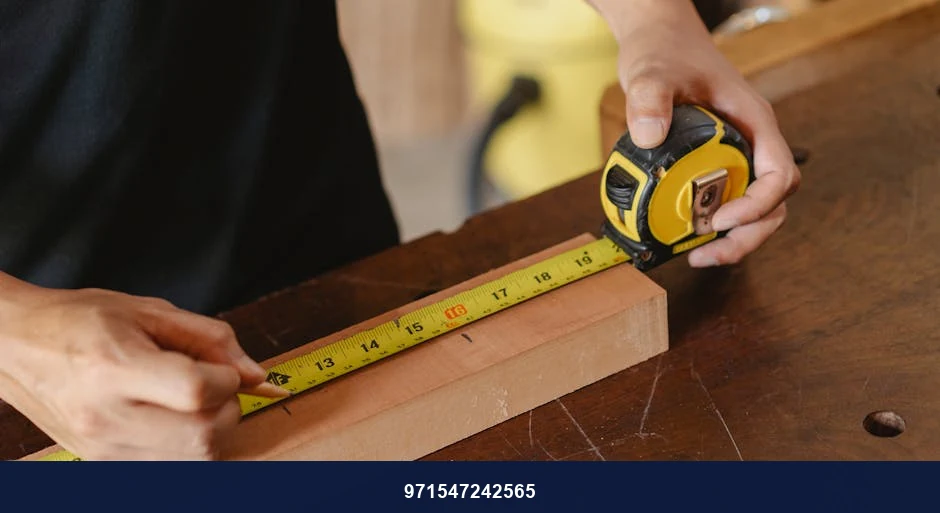 Accurate unrecognizable male worker with pencil and measuring tape on wooden board standing near workbench during work process on blurred background