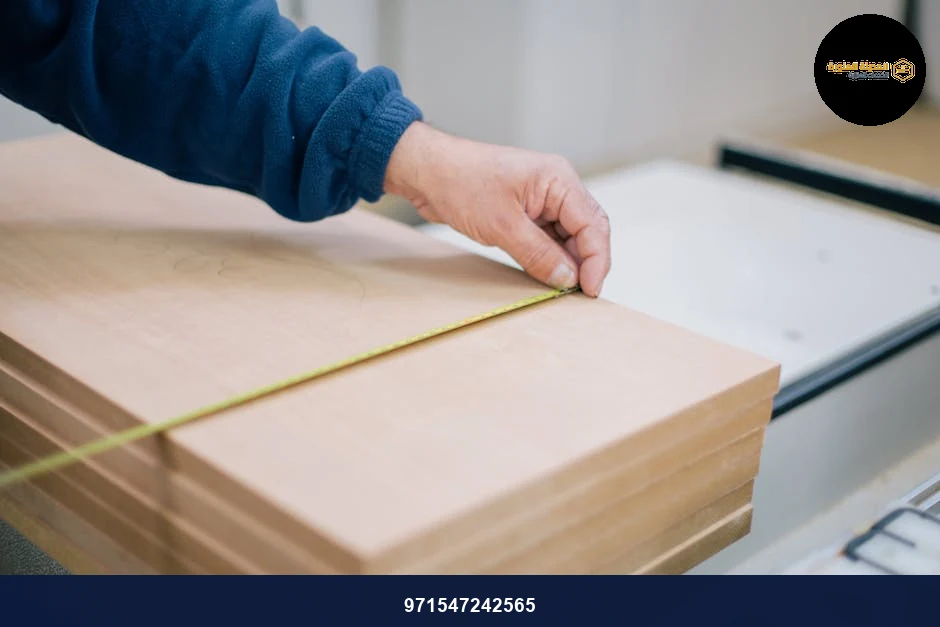 Close-up of a carpenter's hand using a tape measure to measure wooden planks indoors.
