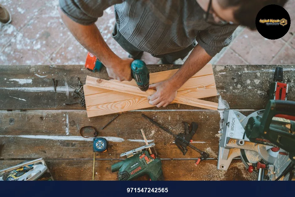 Craftsman busy drilling wooden planks in a carpentry workshop with various tools around.