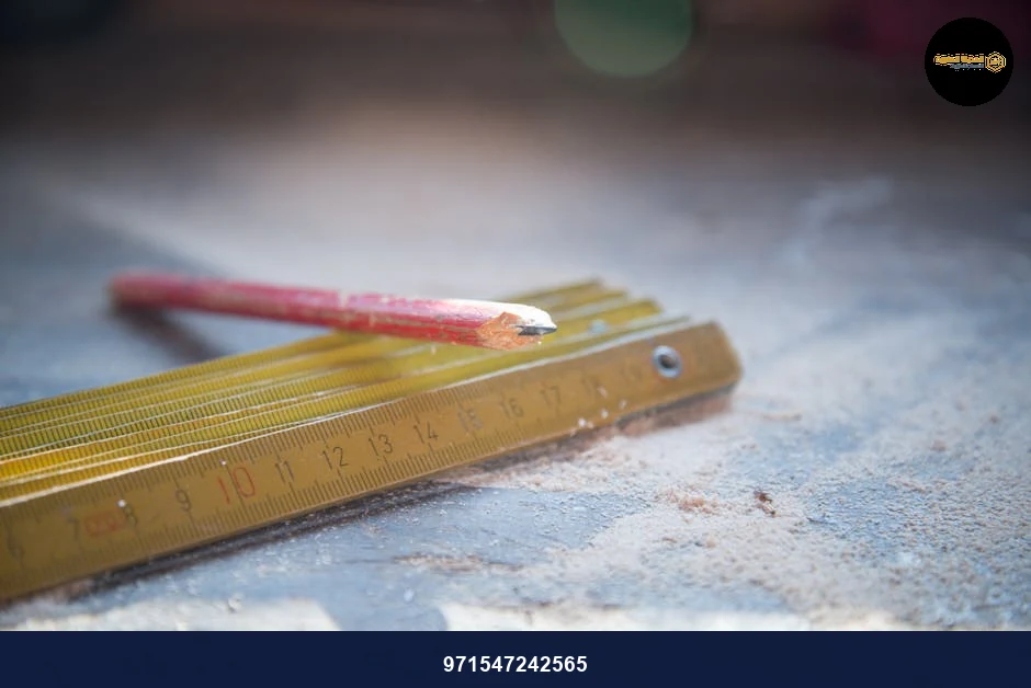 A red pencil and folding ruler on a dusty workshop table, symbolizing craftsmanship.