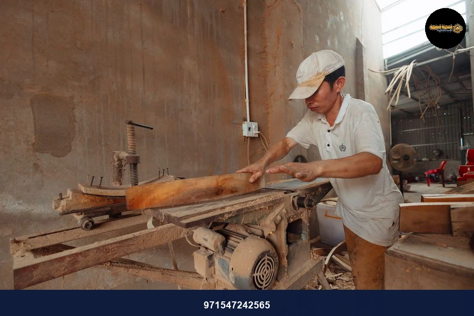 A carpenter in a dusty workshop precisely cuts wood using an industrial saw.