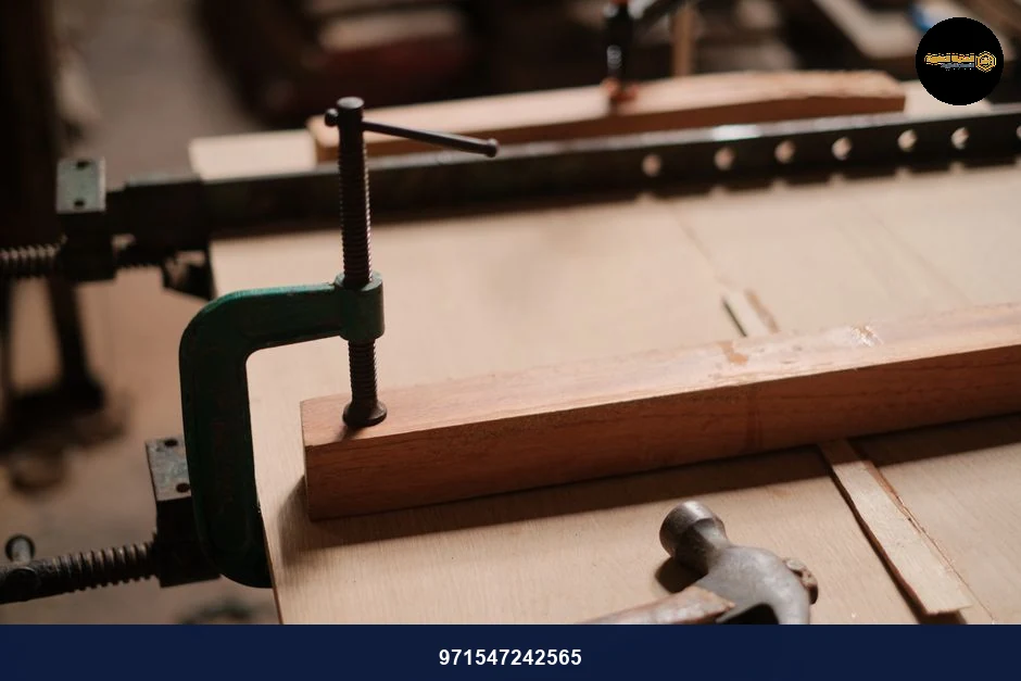 Detailed view of clamps holding wood in place alongside a hammer in a workshop.