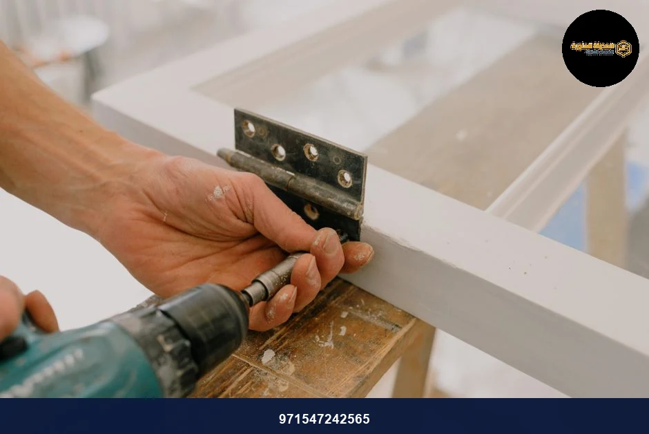Crop unrecognizable worker drilling metal hinge on white window frame during house renovation. Crop unrecognizable worker drilling metal hinge on white window frame during house renovation.
