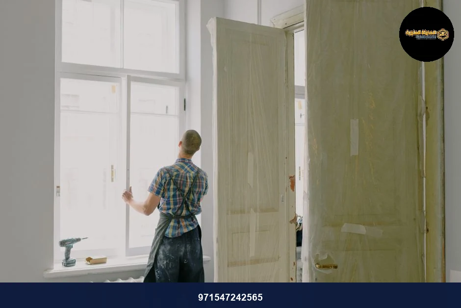 Back view of unrecognizable workman in apron mounting window near drilling machine and doors in flat Back view of unrecognizable workman in apron mounting window near drilling machine and doors in flat