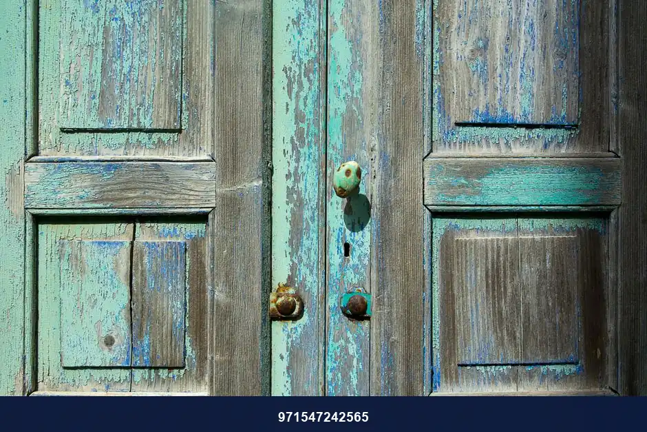 Close-up of weathered wooden doors showcasing rustic blue and turquoise paint texture with vintage doorknob.
